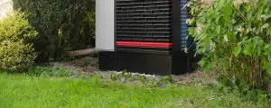 Außeneinheit einer Luft-Wasser-Wärmepumpe neben einem Wohnhaus